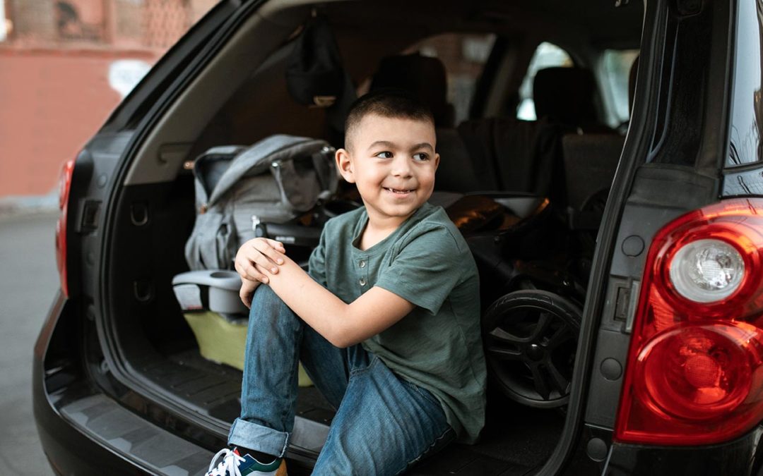 Child sitting in back of open car, smiling, looking toward sidewalk