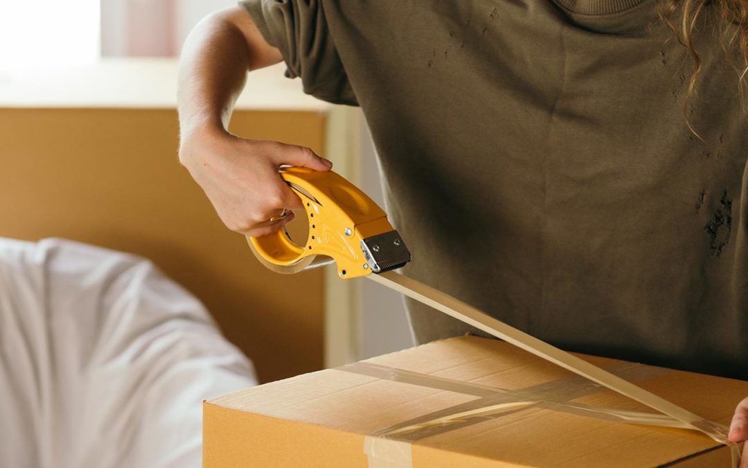 Woman packing a box, putting packing tape on it.